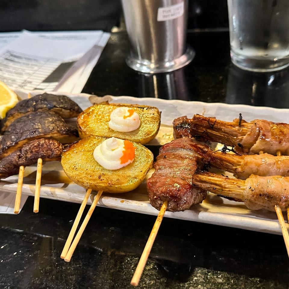 Grilled skewers of meat, mushrooms, and shrimp served with roasted potatoes and creamy toppings on a restaurant platter.