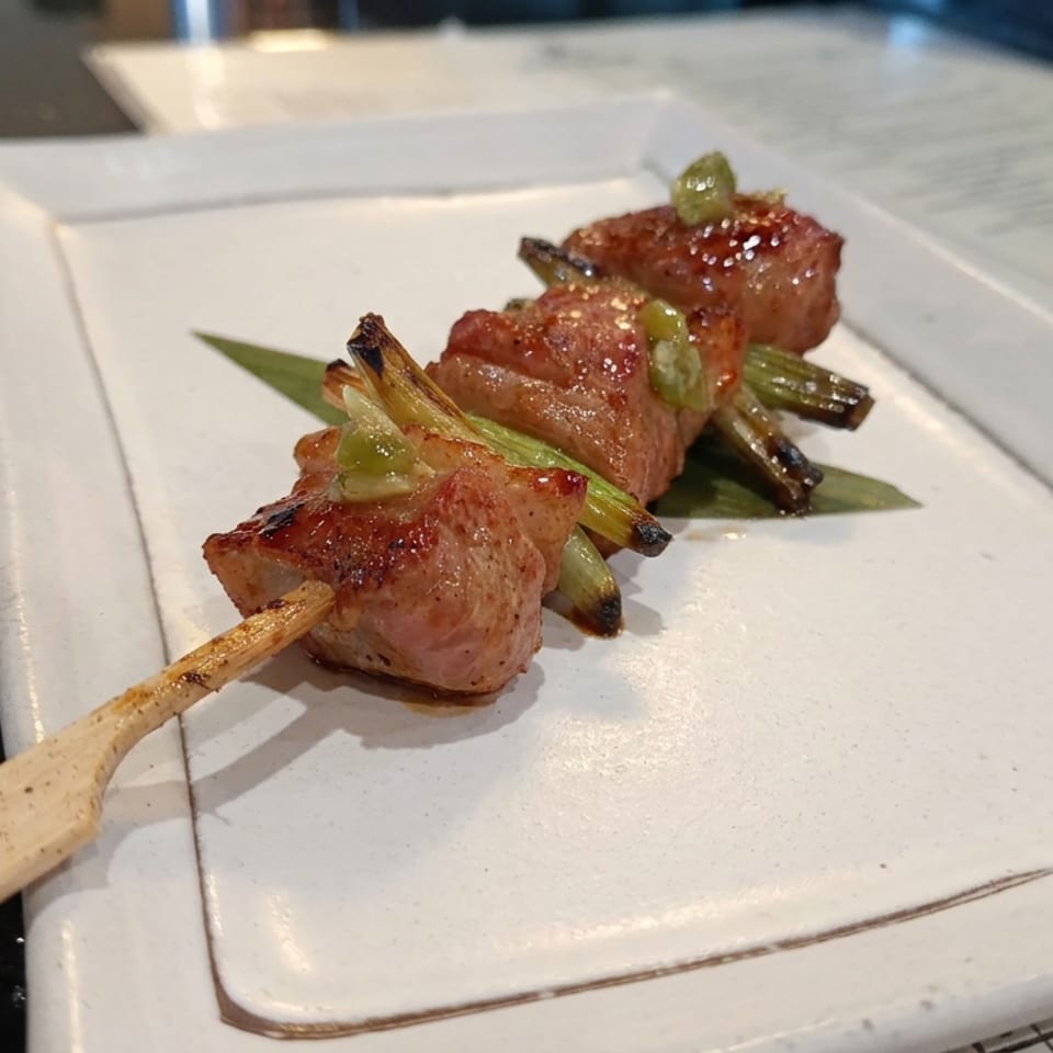 Glazed grilled meat skewers with charred green onions and peppers on a white rectangular plate.
